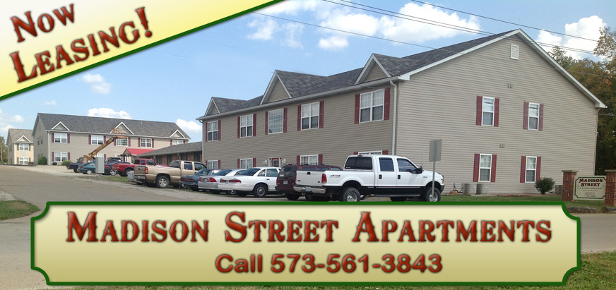A photo of an tan colored apartmet complex with many cars parked in front. There is a graphic over the corner with the words: Now Leasing! Along the bottom of the image is a beige colored graphic with red text:
	Madison Street Call 573-561-3843